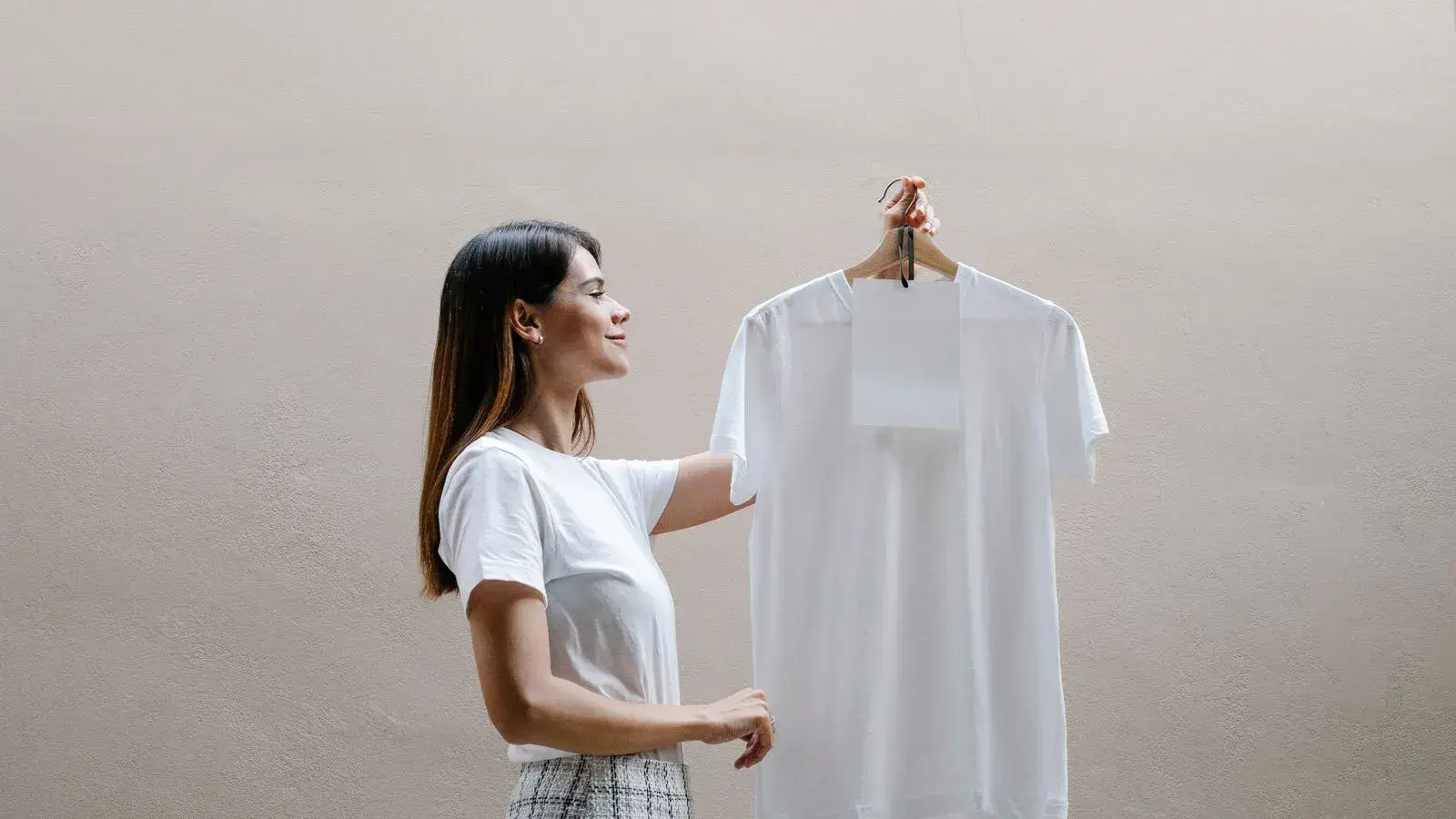 Woman holding a plain white T-shirt on a hanger against a neutral wall