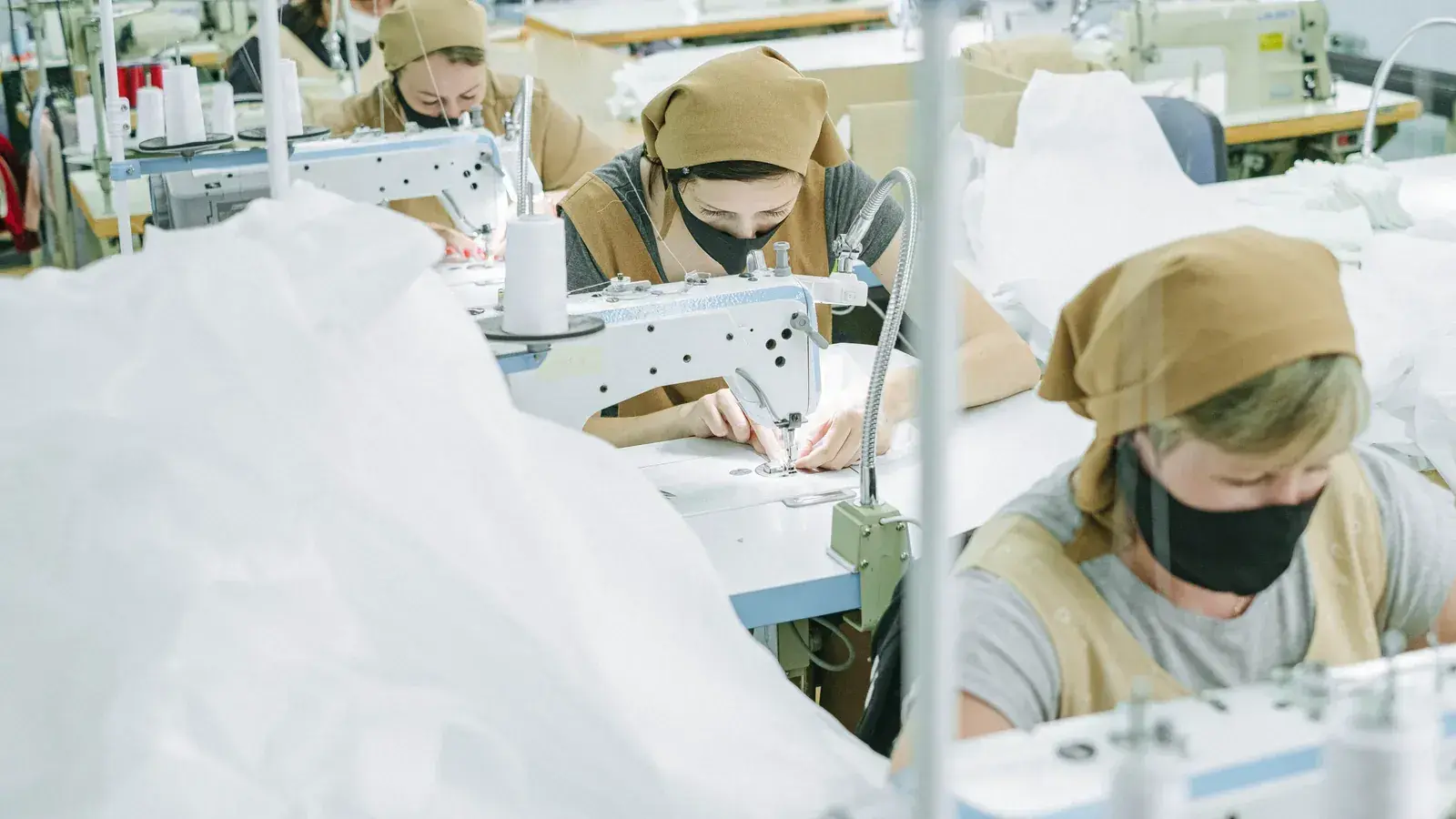 Rows of industrial sewing machines with operators working on light-colored garments