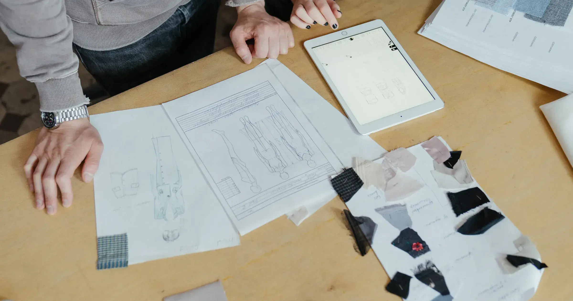 Apparel product developers reviewing garment sketches, fabric swatches and a digital sample brief