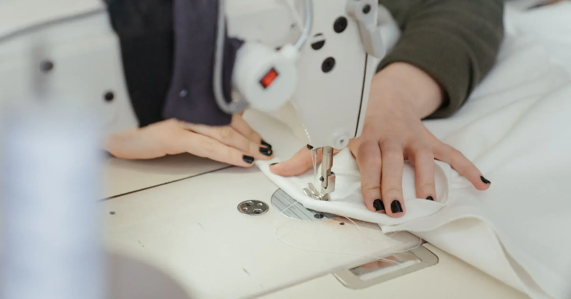 Close-up of hands sewing white fabric on an industrial sewing machine