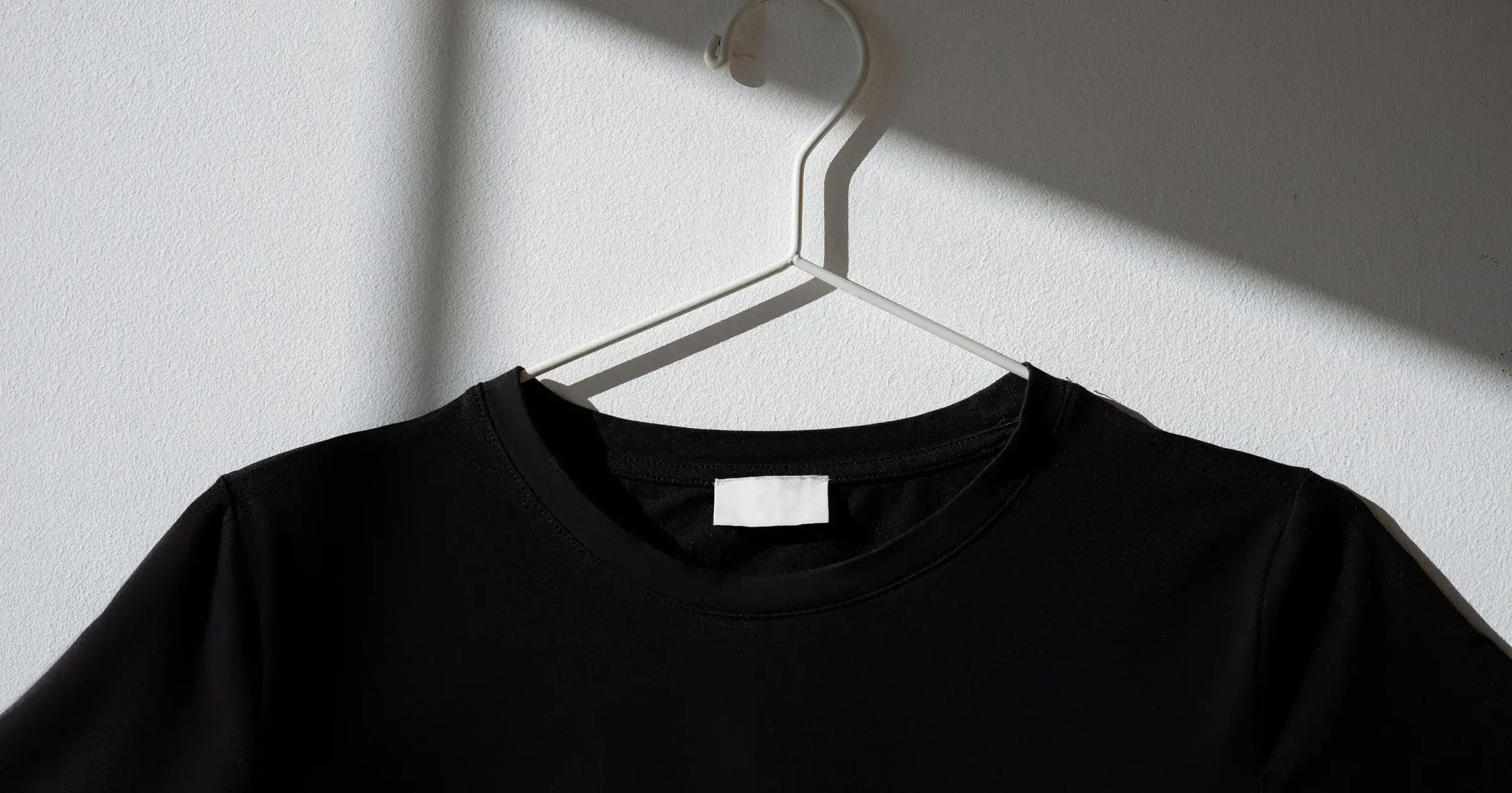 A black t-shirt with a blank white label hanging against a white wall