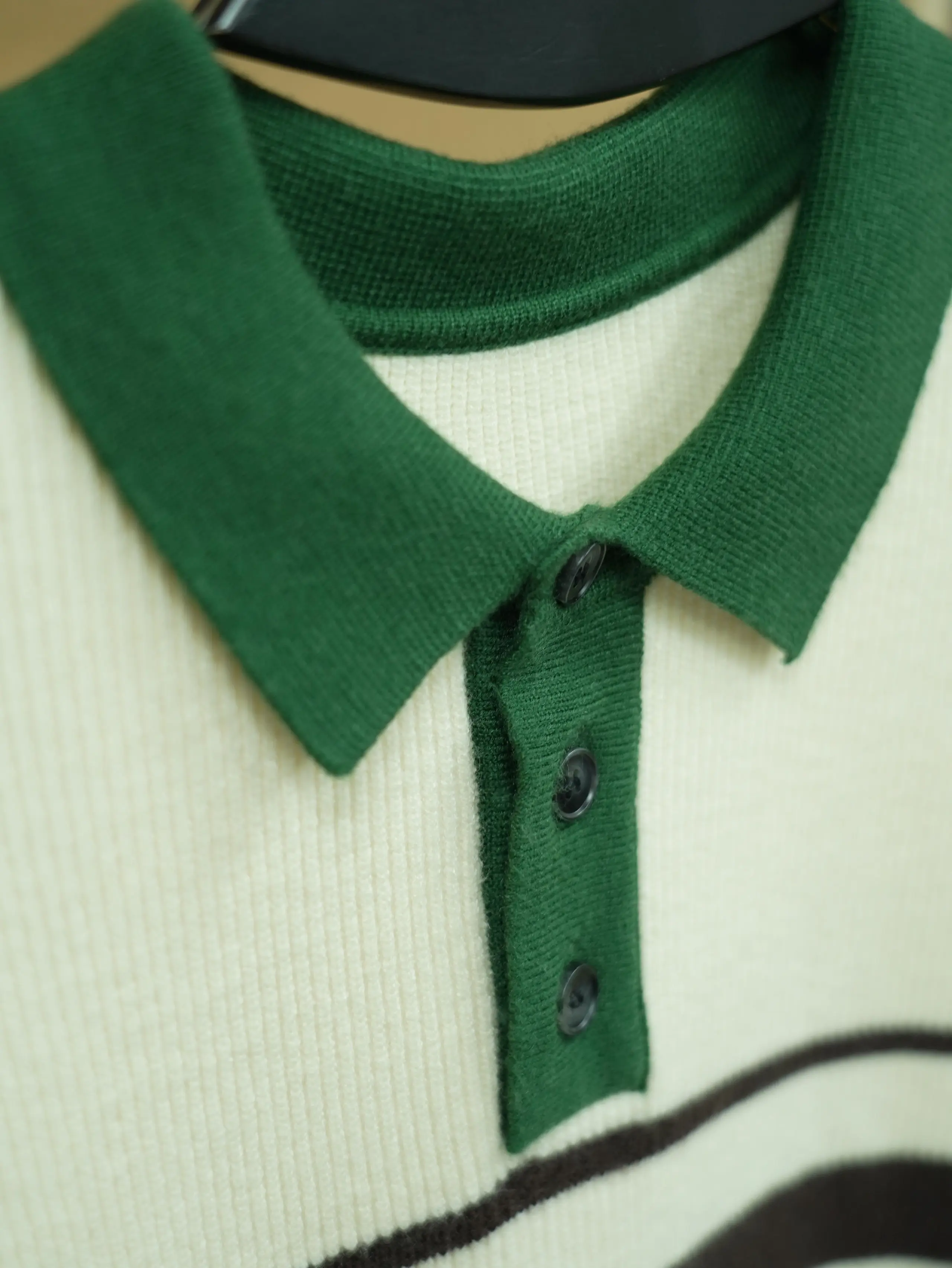 Close-up of an ivory rib-knit polo with a forest-green collar and button placket for a smart-casual capsule