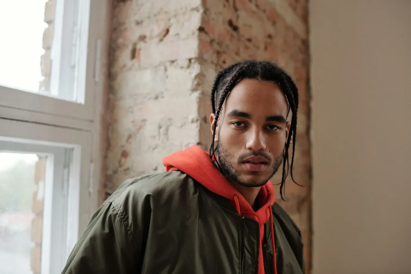 Man in an olive nylon bomber jacket layered over a red hooded sweatshirt