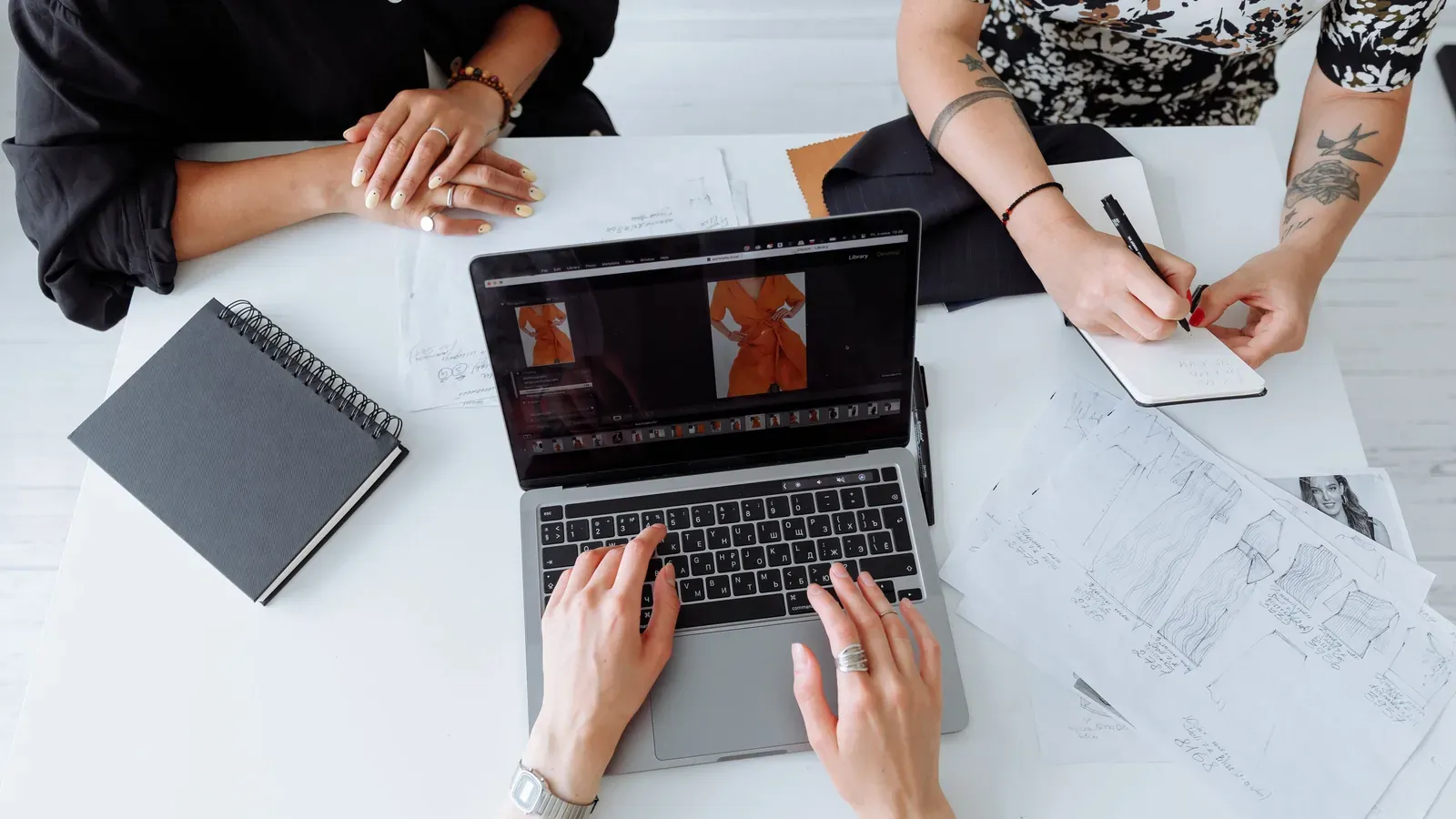 Product development team reviewing garment documents and a sample schedule on a laptop