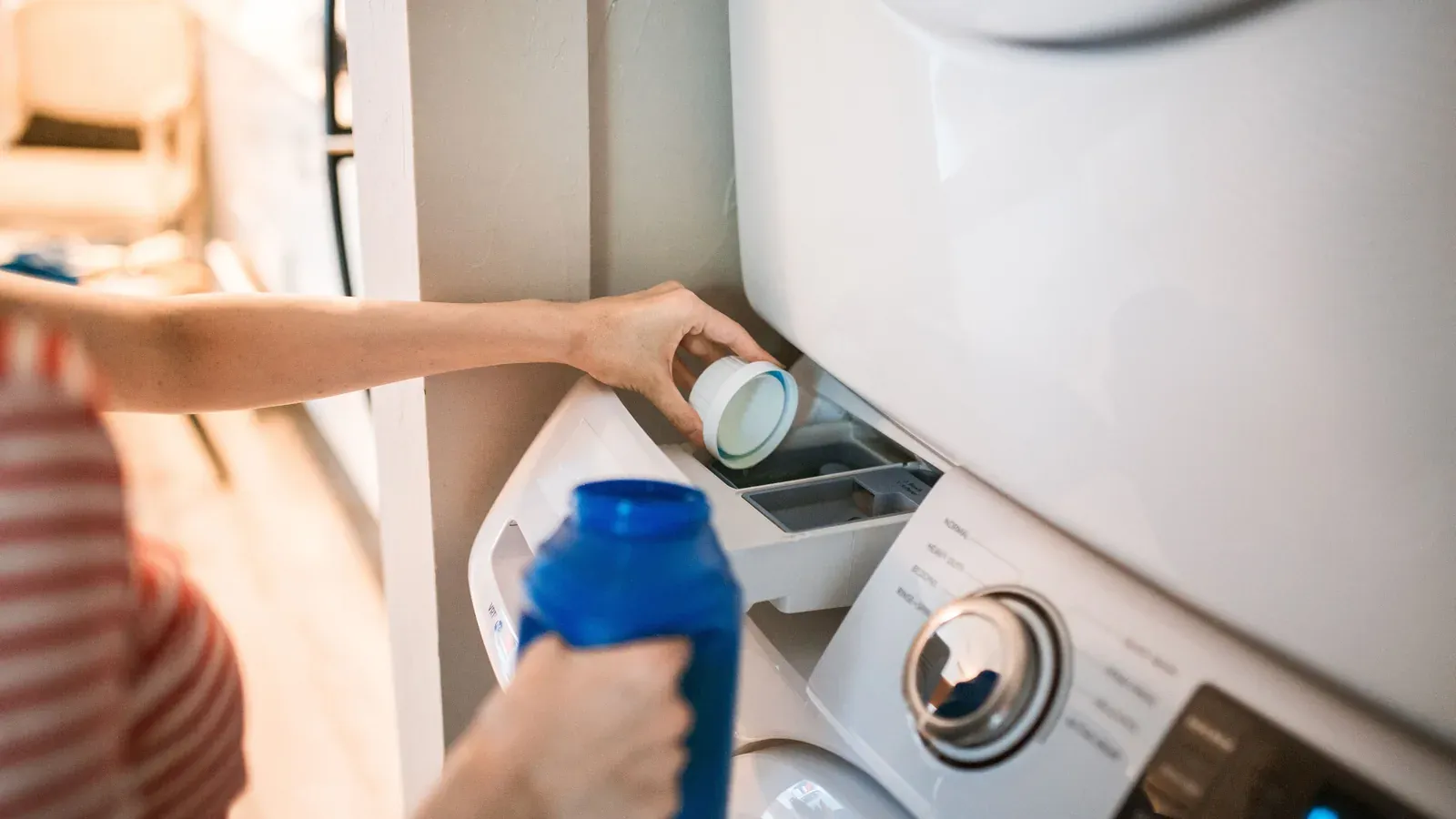 A person pouring detergent into the dispenser of a front-loading washing machine