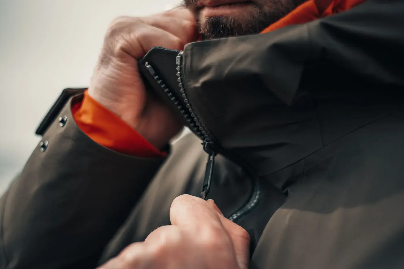 Hands zipping up a dark winter jacket with a bright lining
