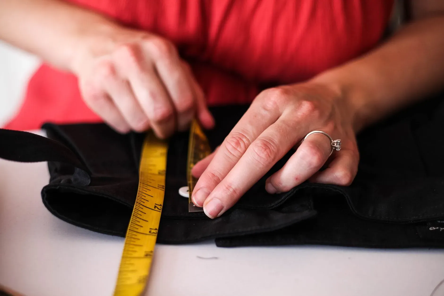 Hands measuring a black garment detail with a yellow tape measure