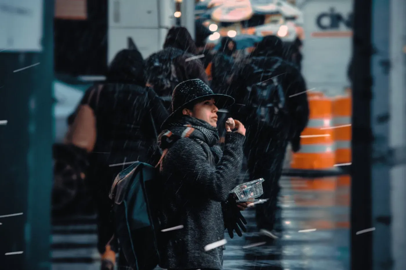 Person in a dark jacket standing on a rainy city street at night