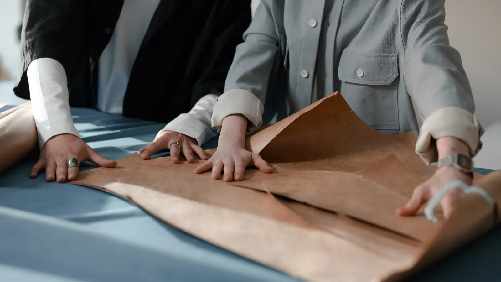 Two pattern makers aligning paper pattern pieces over fabric on a cutting table