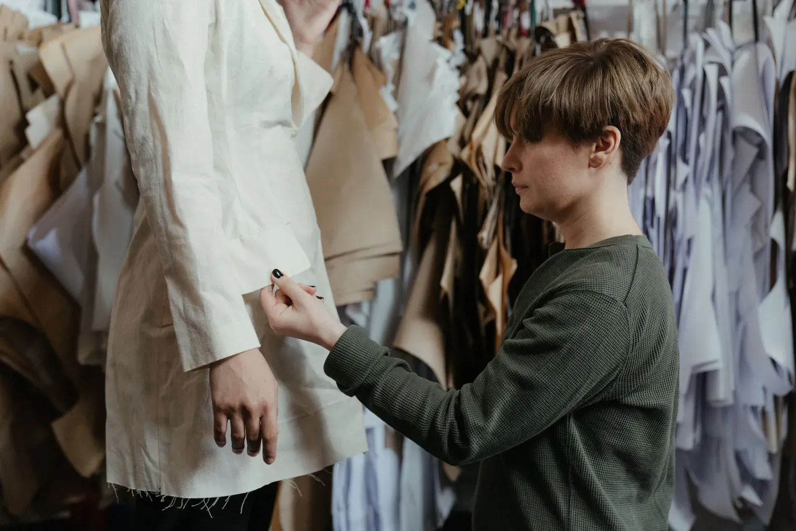 A tailor pinning the sleeve of a garment on a mannequin, with fabric pieces hanging in the background