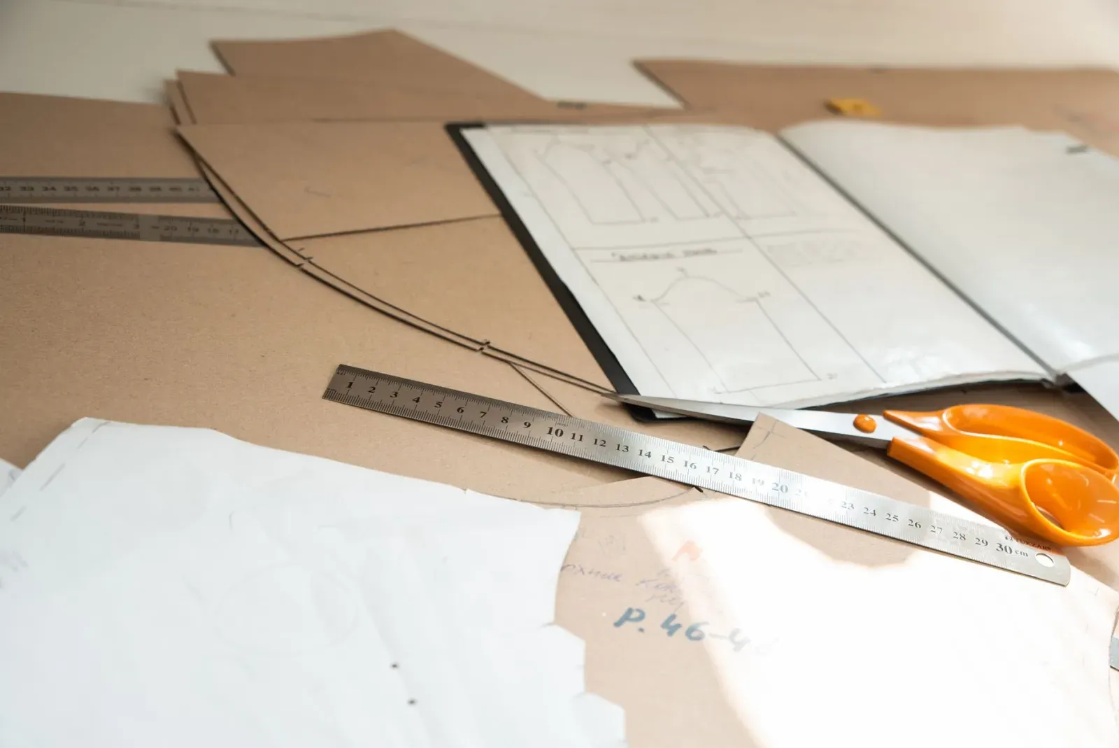Paper garment patterns, rulers and scissors arranged on a pattern-cutting table