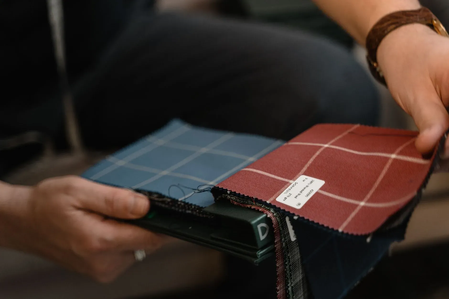 Hands comparing plaid fabric swatches in a sample book