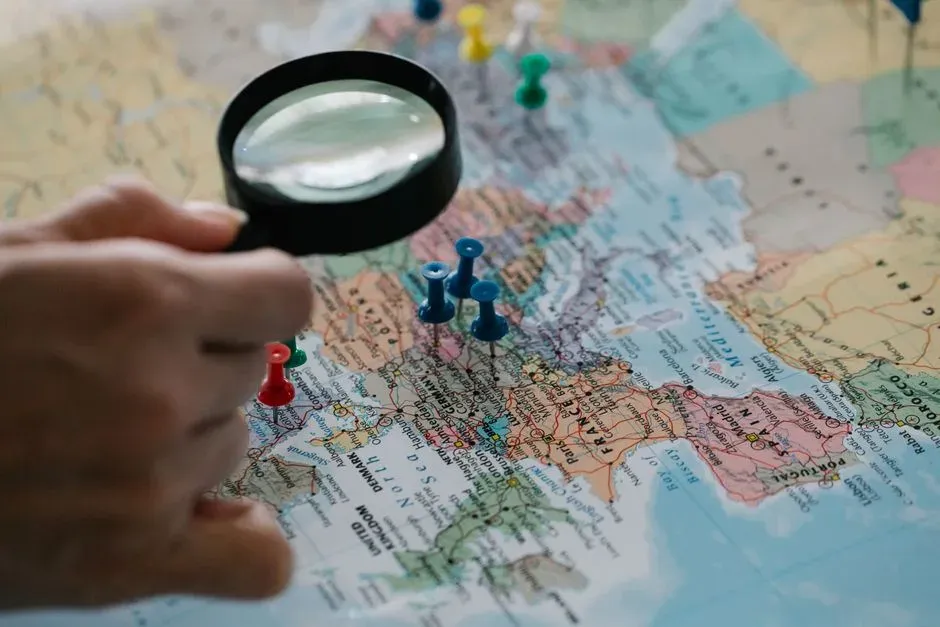 A hand holding a magnifying glass over a map with push pins