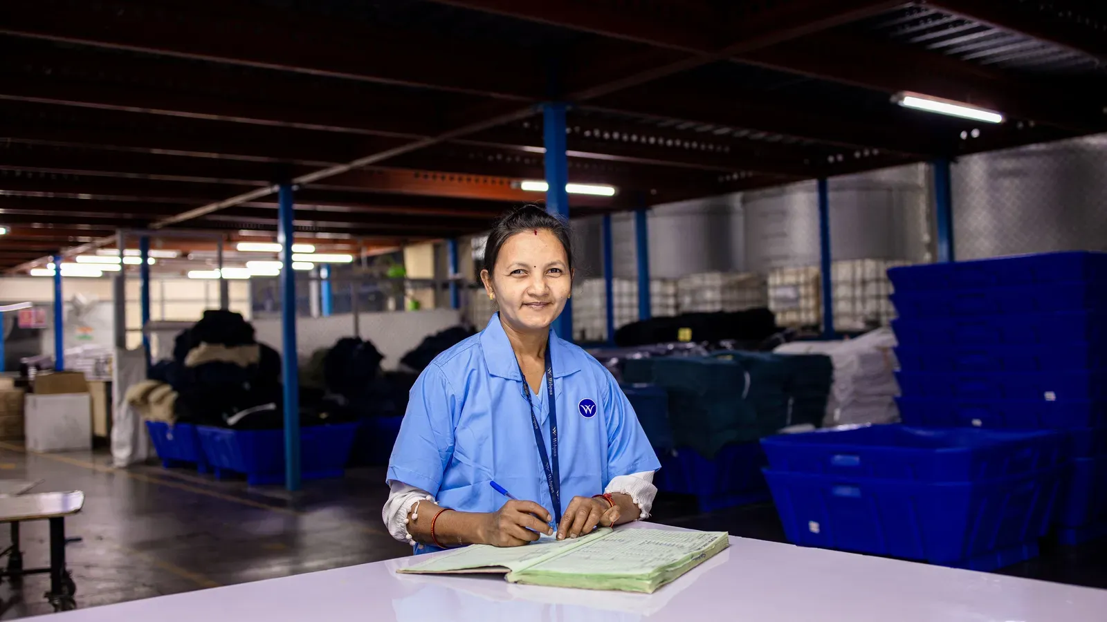 A worker recording details in a ledger at a table inside a textile warehouse