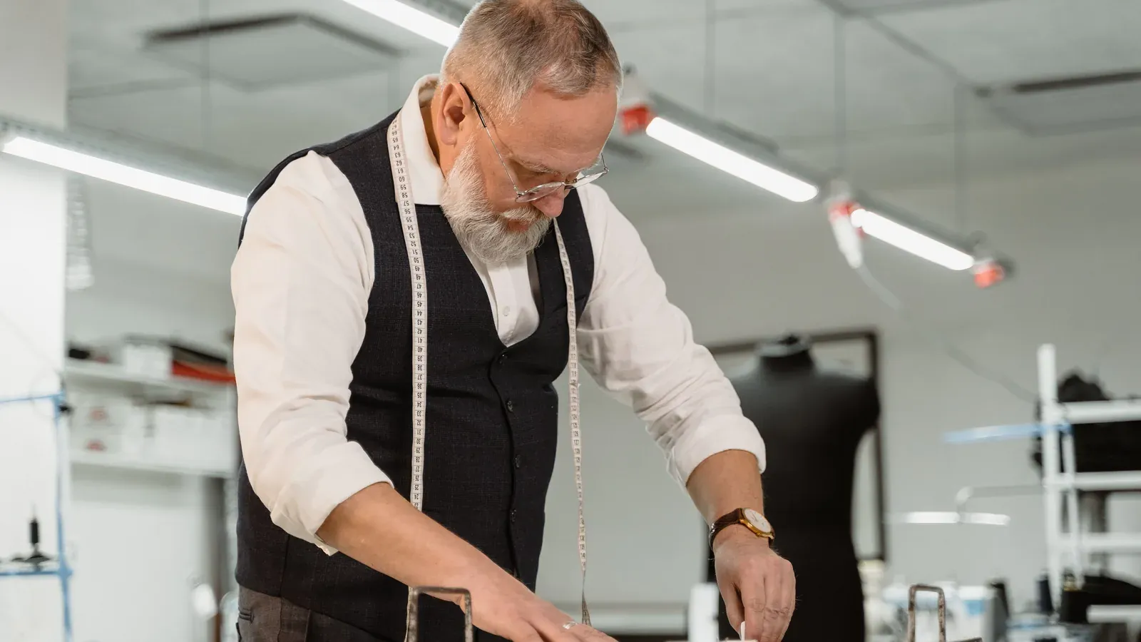 A tailor measuring fabric laid out on a studio worktable