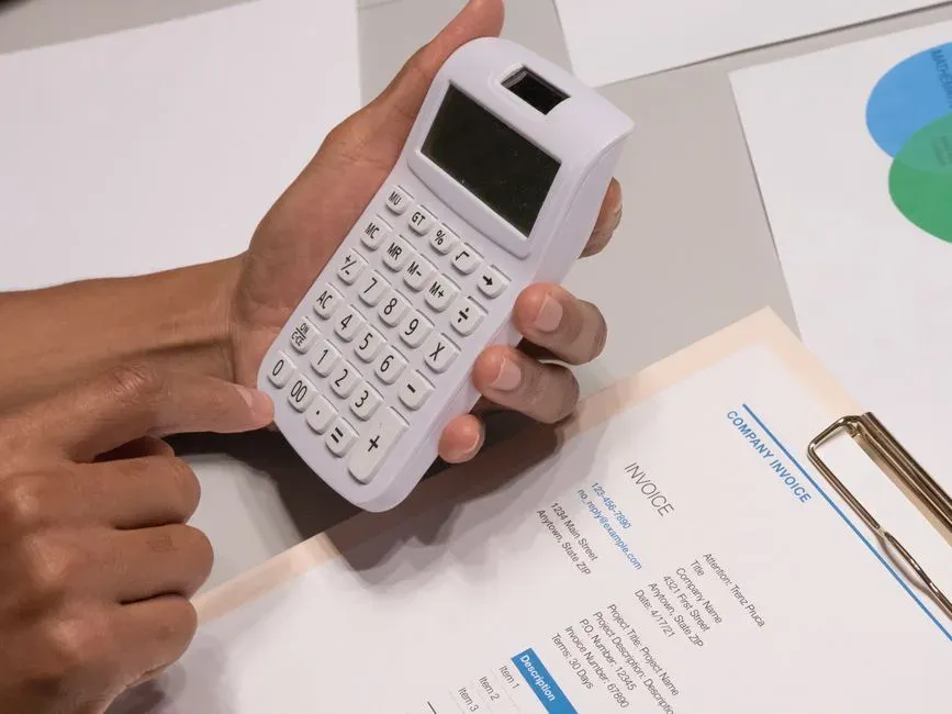 Hands holding a calculator over an invoice document