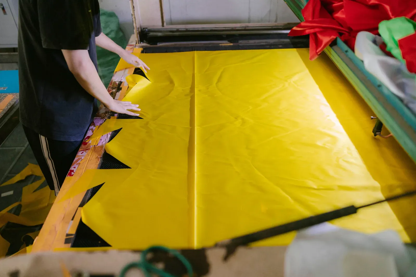 A person cutting a length of yellow fabric on a large cutting table in a workshop