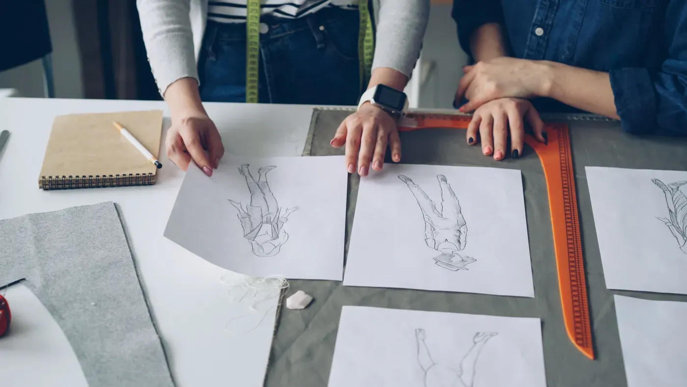 Two designers reviewing garment sketches, a pattern ruler and a tape measure on a worktable
