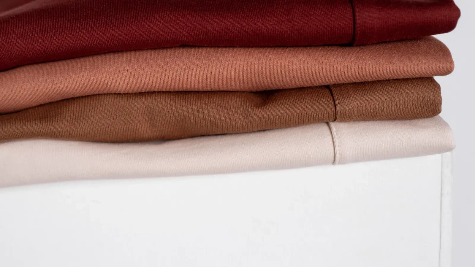 A stack of folded plain knit garments in four colors on a white surface