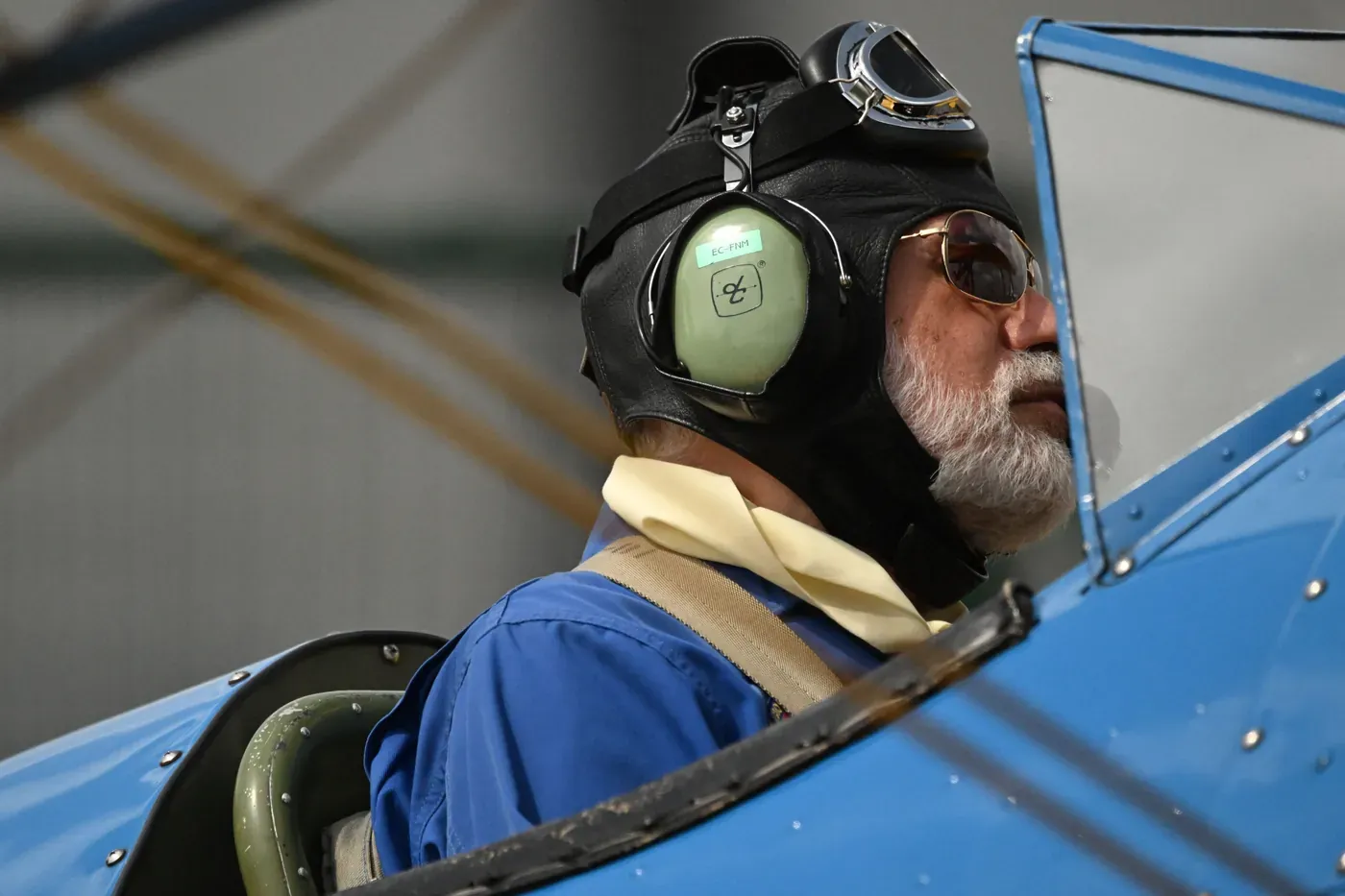 Aviator in a leather flying helmet and goggles seated in an open vintage aircraft cockpit