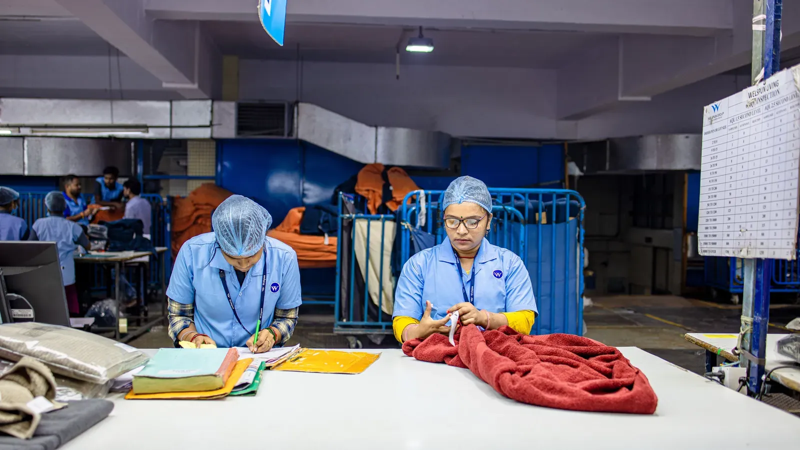 Two textile workers checking fabric against paperwork at an inspection table