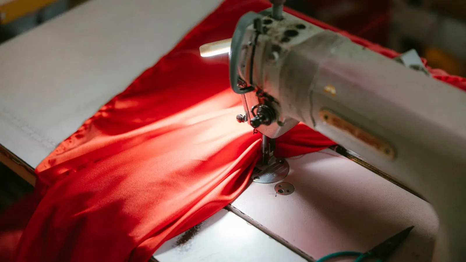 Industrial sewing machine stitching red fabric under a work light
