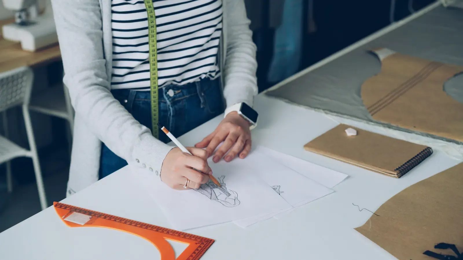 Fashion designer sketching a garment beside paper patterns and measuring tools