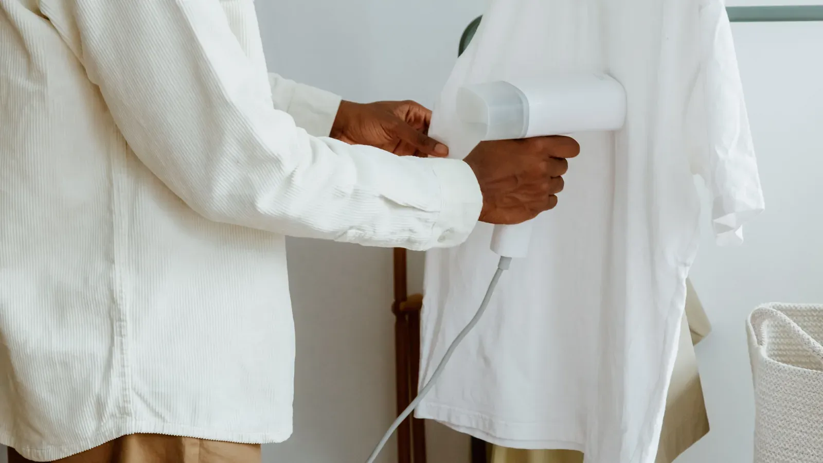 A person steam-pressing a white shirt hanging on a clothing rack