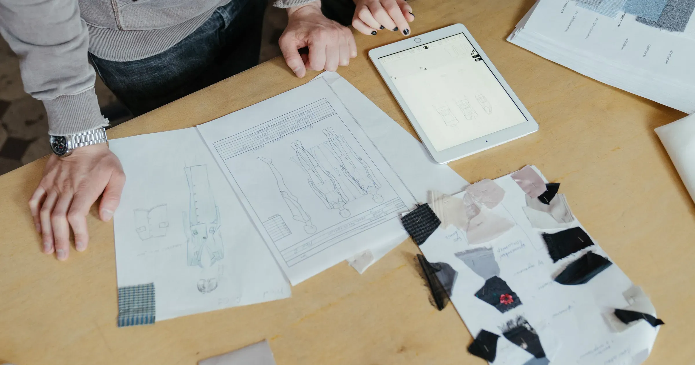 Apparel product developers reviewing garment sketches, fabric swatches and a digital sample brief