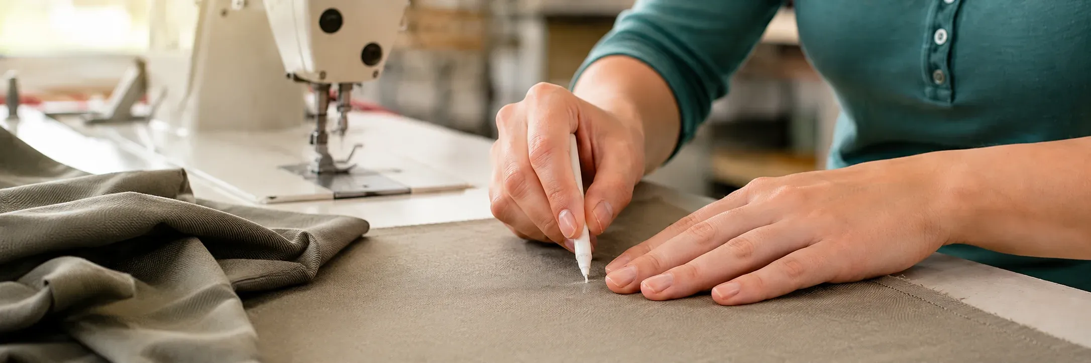 Hands marking fabric beside an industrial sewing machine