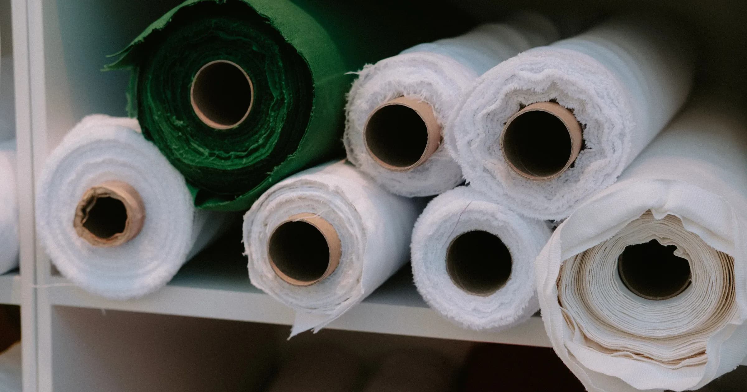 Rolls of folded fabric in different colors stacked on a warehouse shelf
