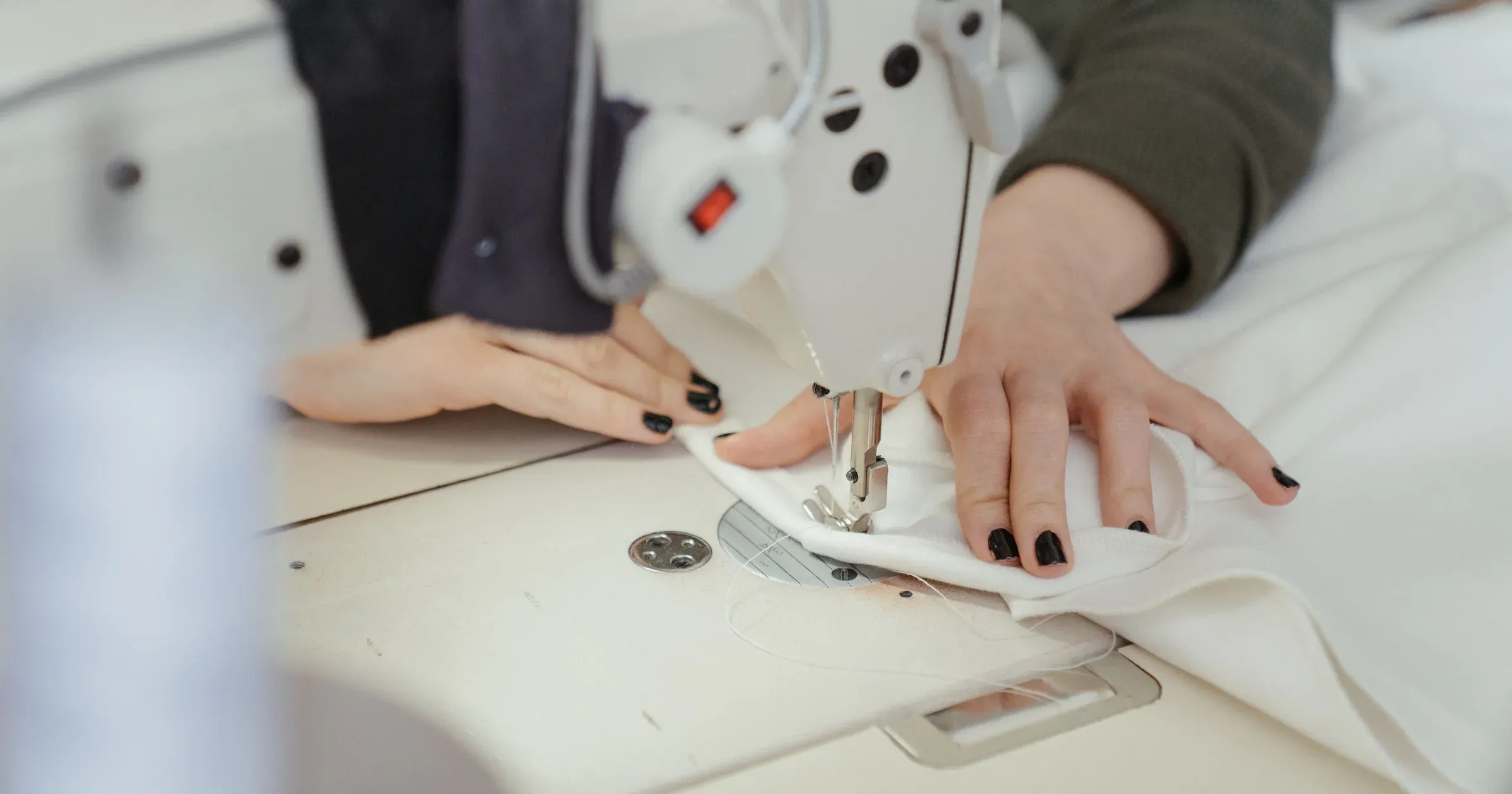 Close-up of hands sewing white fabric on an industrial sewing machine