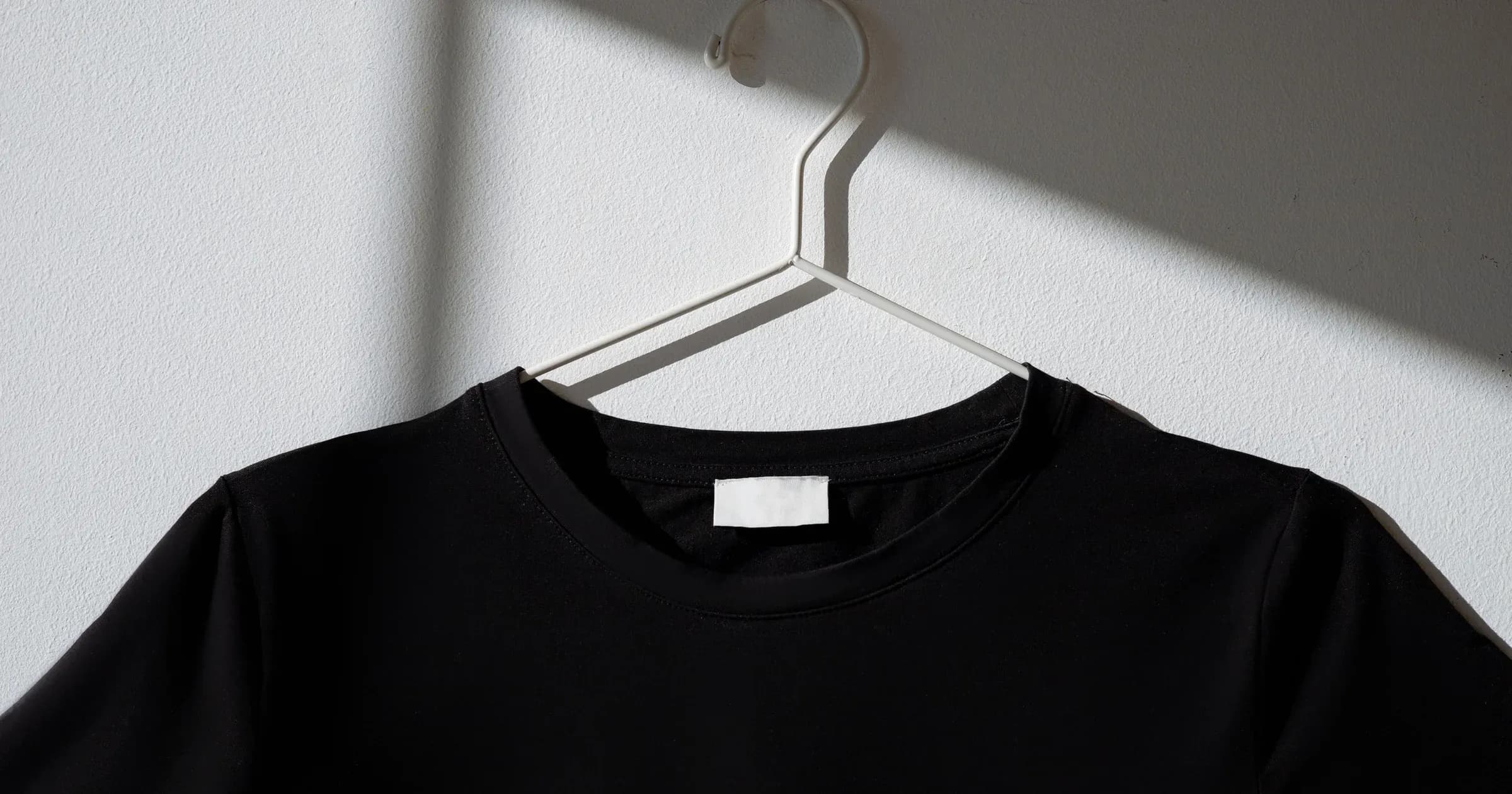 A black t-shirt with a blank white label hanging against a white wall