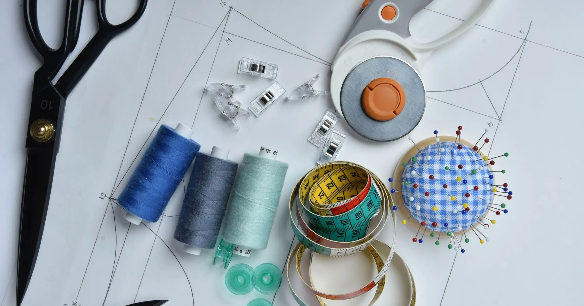 Sewing tools, thread, measuring tape and pins arranged on paper garment patterns
