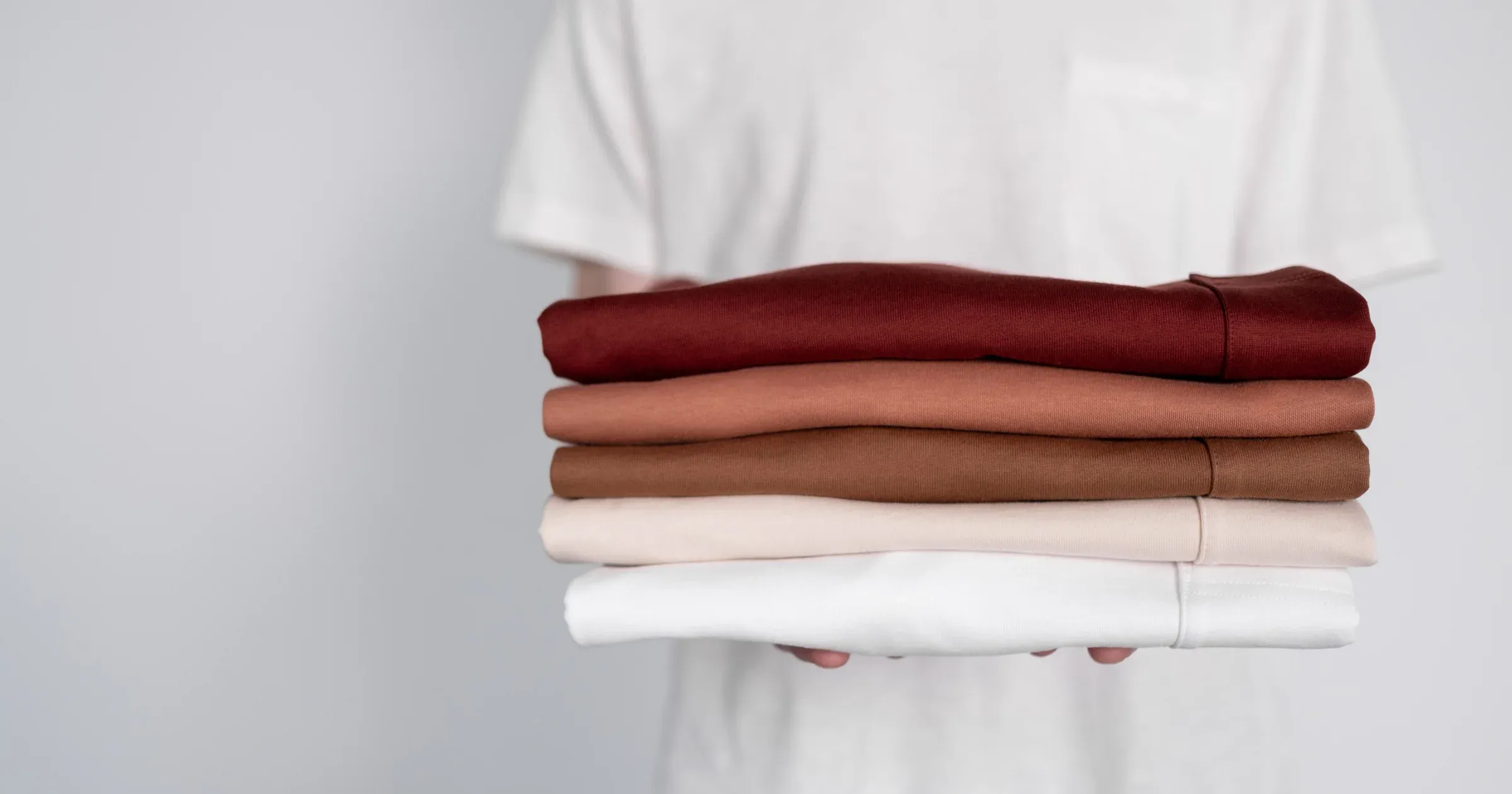 A person holding a stack of neatly folded shirts in earthy tones