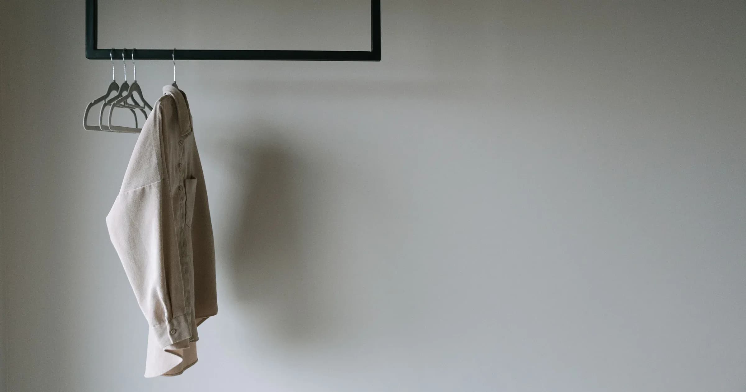 A beige overshirt hanging on a minimalist metal clothing rack