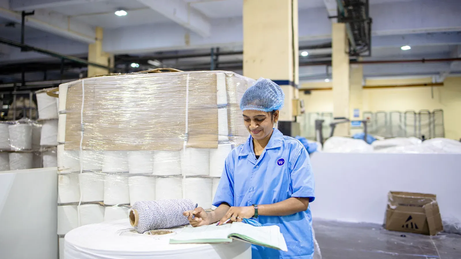 Factory worker documenting production data in a notebook beside material rolls