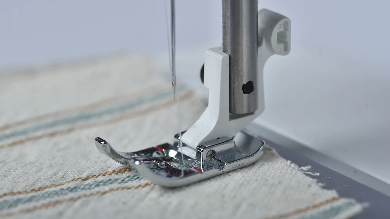 Close-up of a sewing machine needle and presser foot stitching fabric