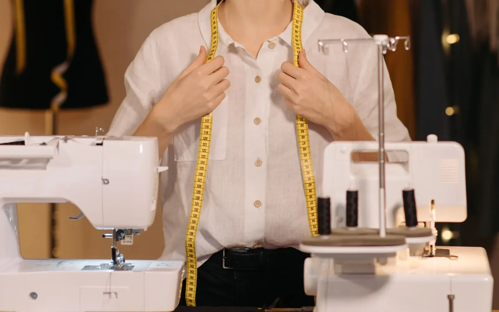 Tailor with a measuring tape standing between sewing machines