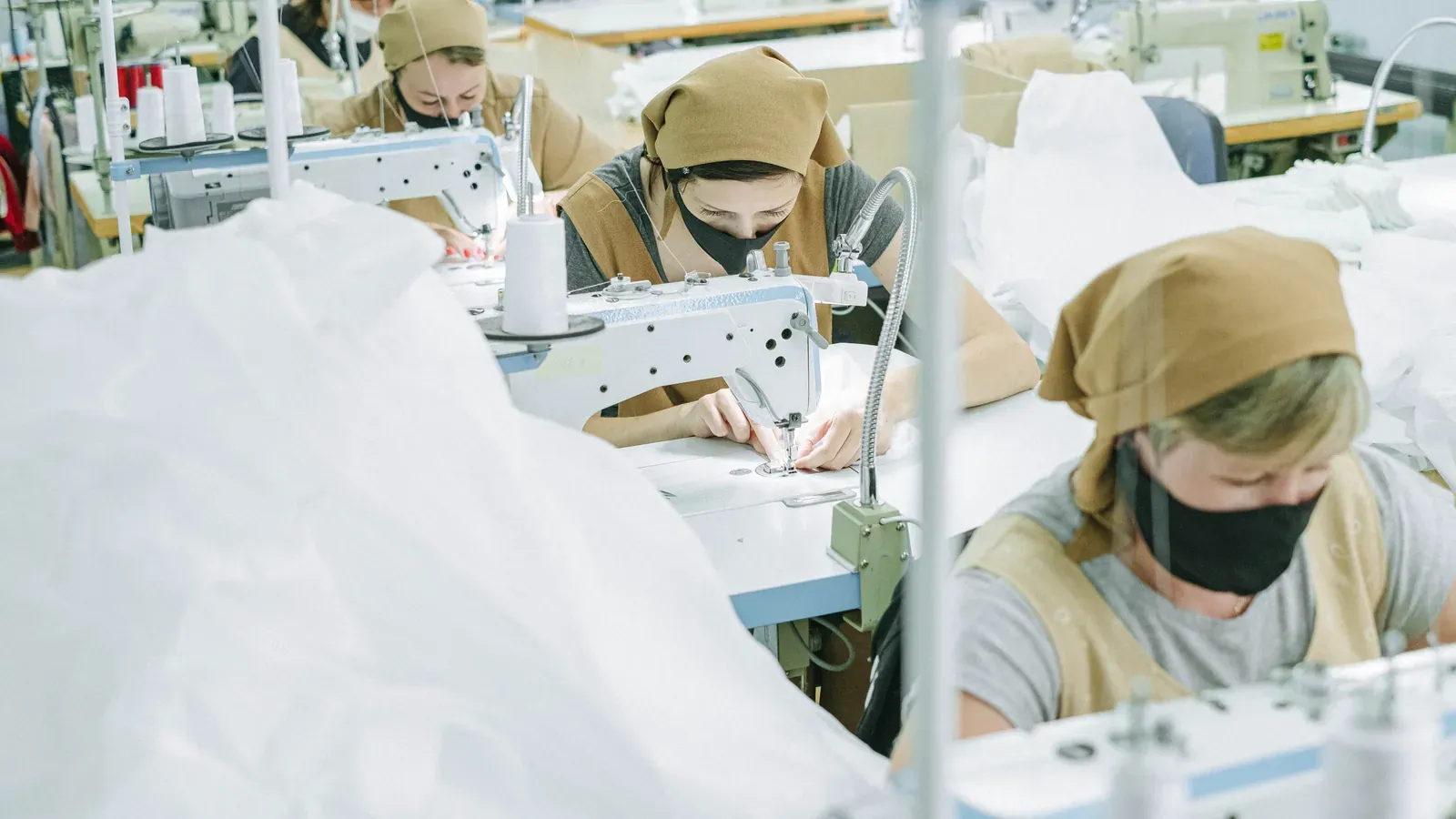 Rows of industrial sewing machines with operators working on light-colored garments
