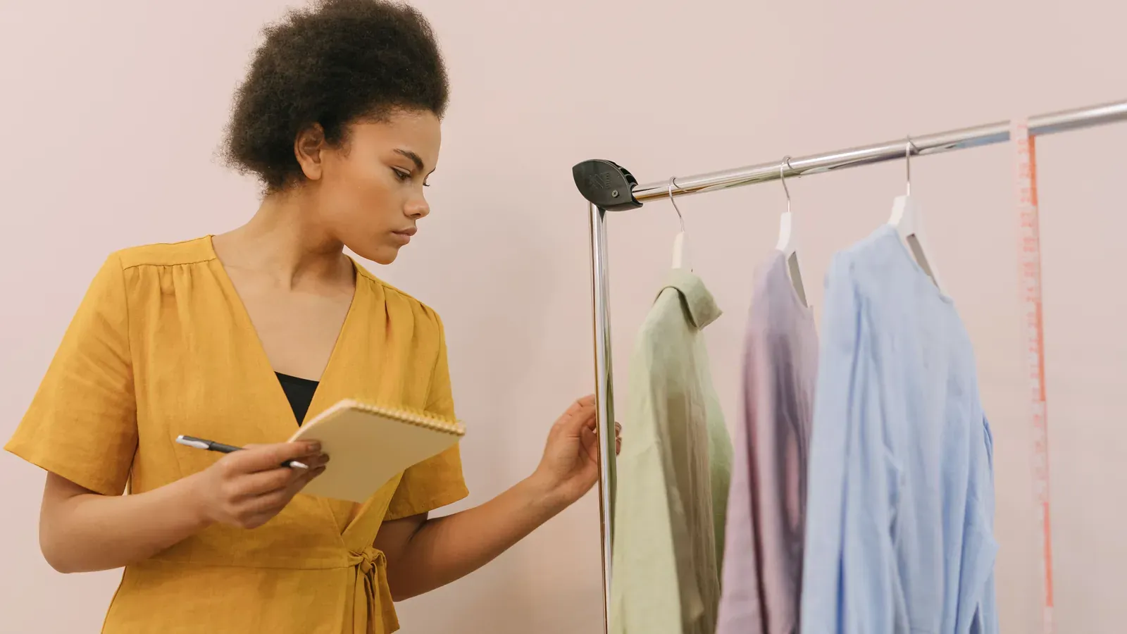 A person in a yellow dress taking notes beside a rack of pastel shirts