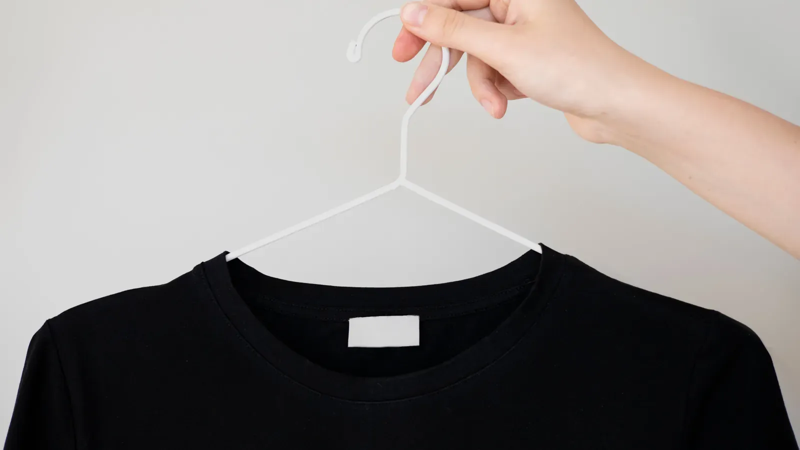 A hand holding a hanger with a plain black t-shirt and a blank neck label