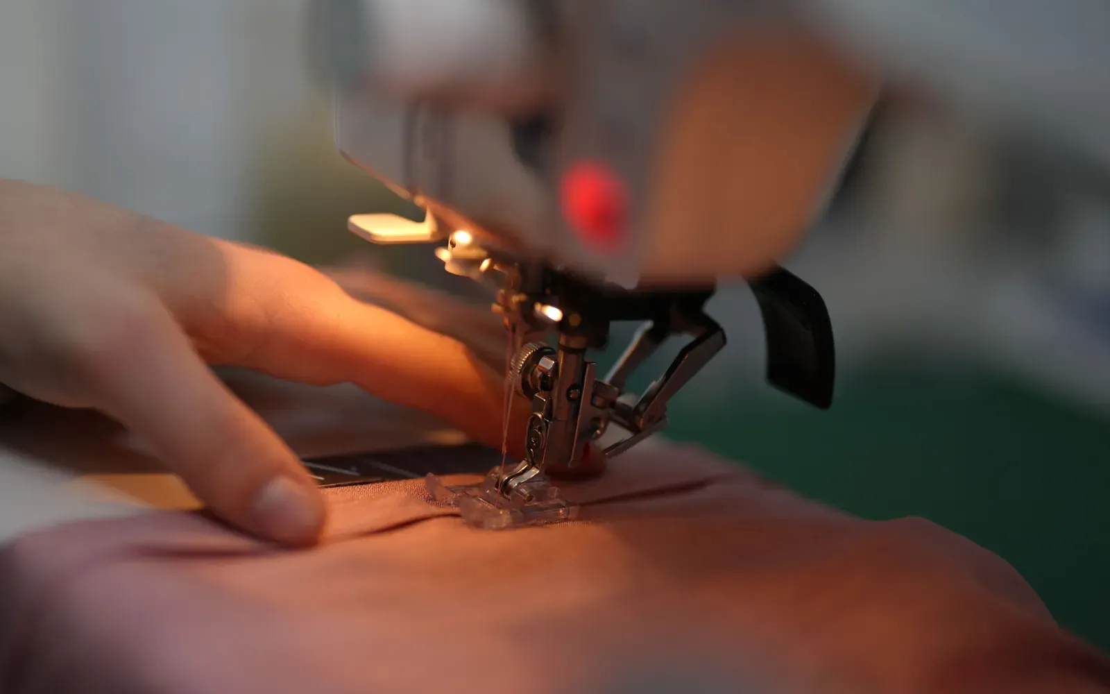 Hands guiding fabric under a sewing machine presser foot
