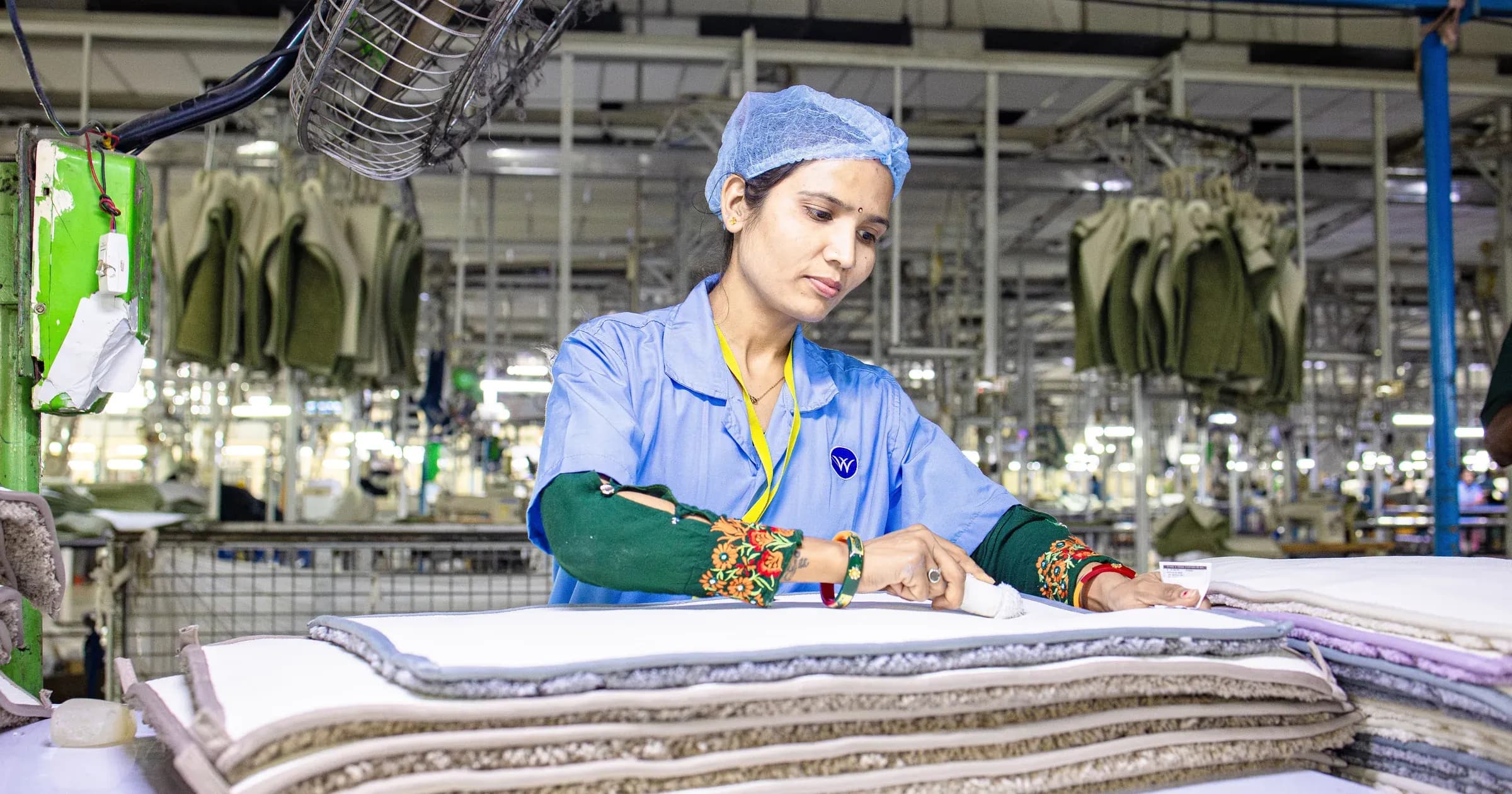 Factory quality controller inspecting folded fabric stacks beside hanging garments