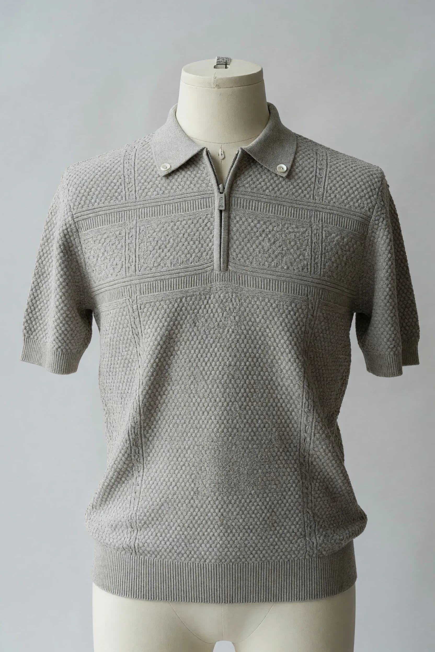 Light-stone short-sleeve knit polo with half-zip collar, geometric chest panel and textured body shown on a faceless mannequin for private-label sourcing