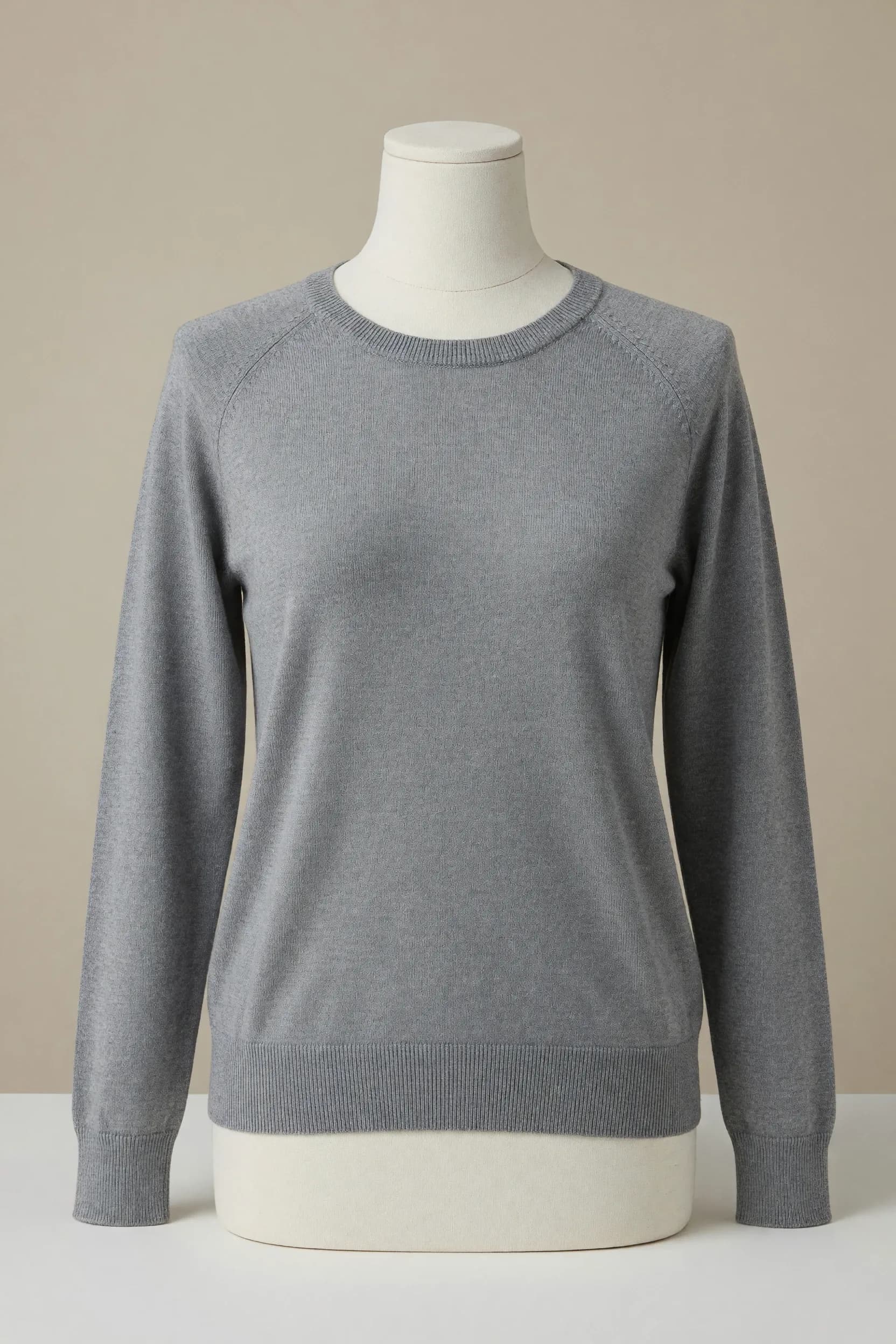 Silver-grey long-sleeve crewneck sweater with visible raglan seams and fine ribbed cuffs and hem on a torso mannequin for private-label knitwear development